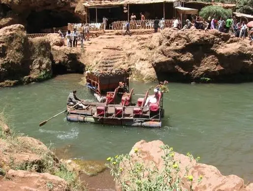 Une barge en bois décorée transportant des passagers sur une rivière aux eaux vertes au pied des falaises d'Ouzoud.
