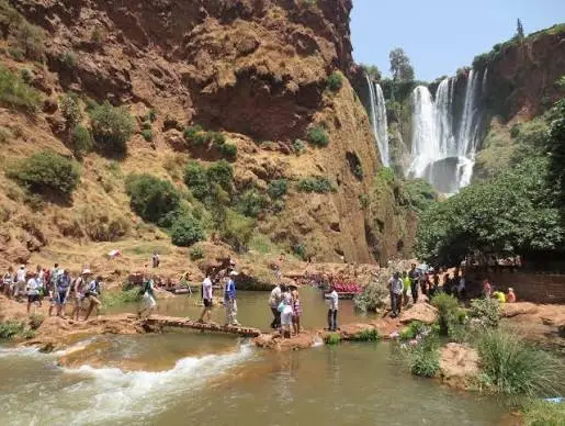 Vue d'ensemble des cascades d'Ouzoud au Maroc, avec des touristes marchant sur un pont au premier plan.