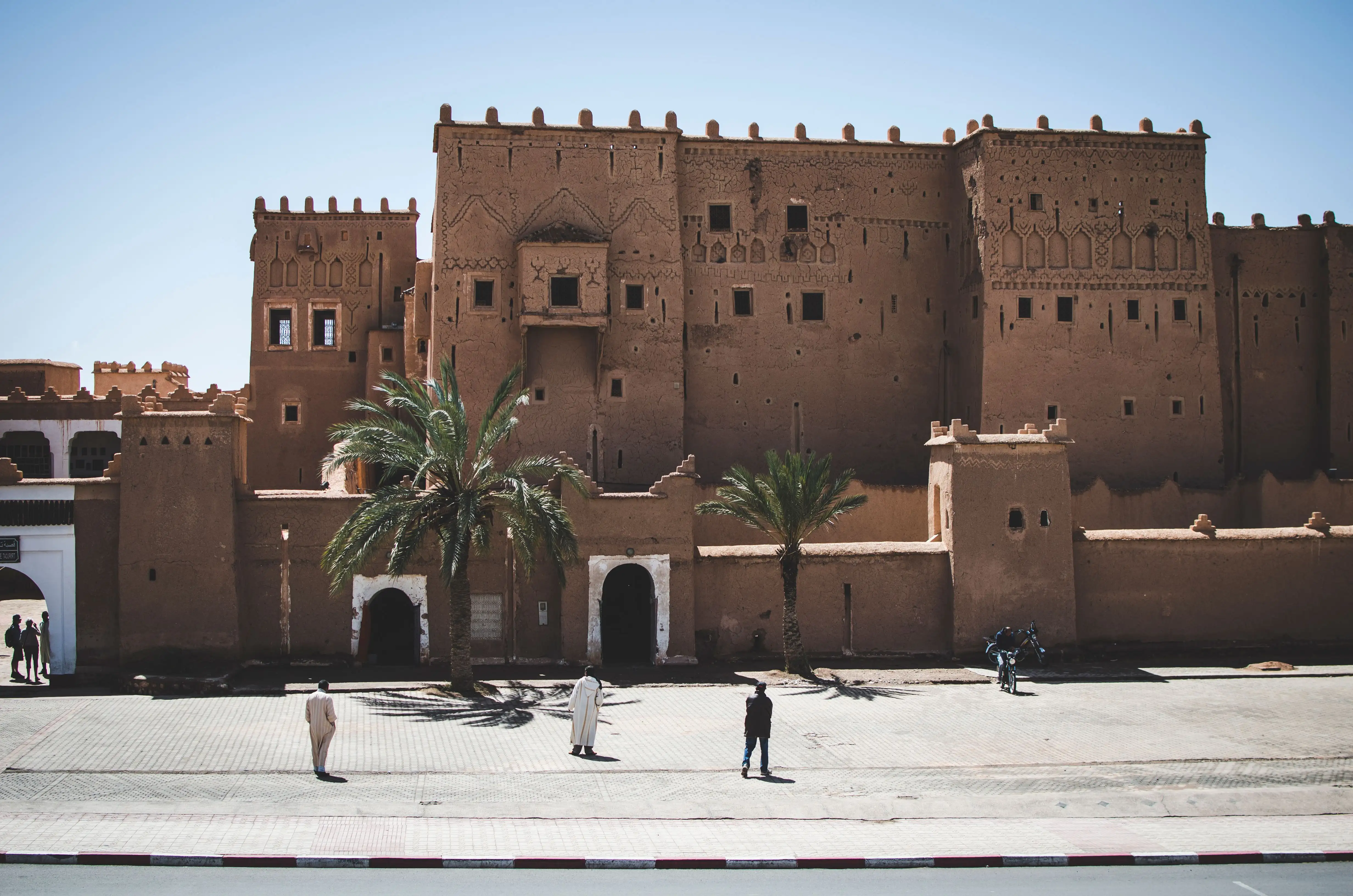 Grande kasbah en terre cuite de Taourirt à Ouarzazate avec palmiers et passants