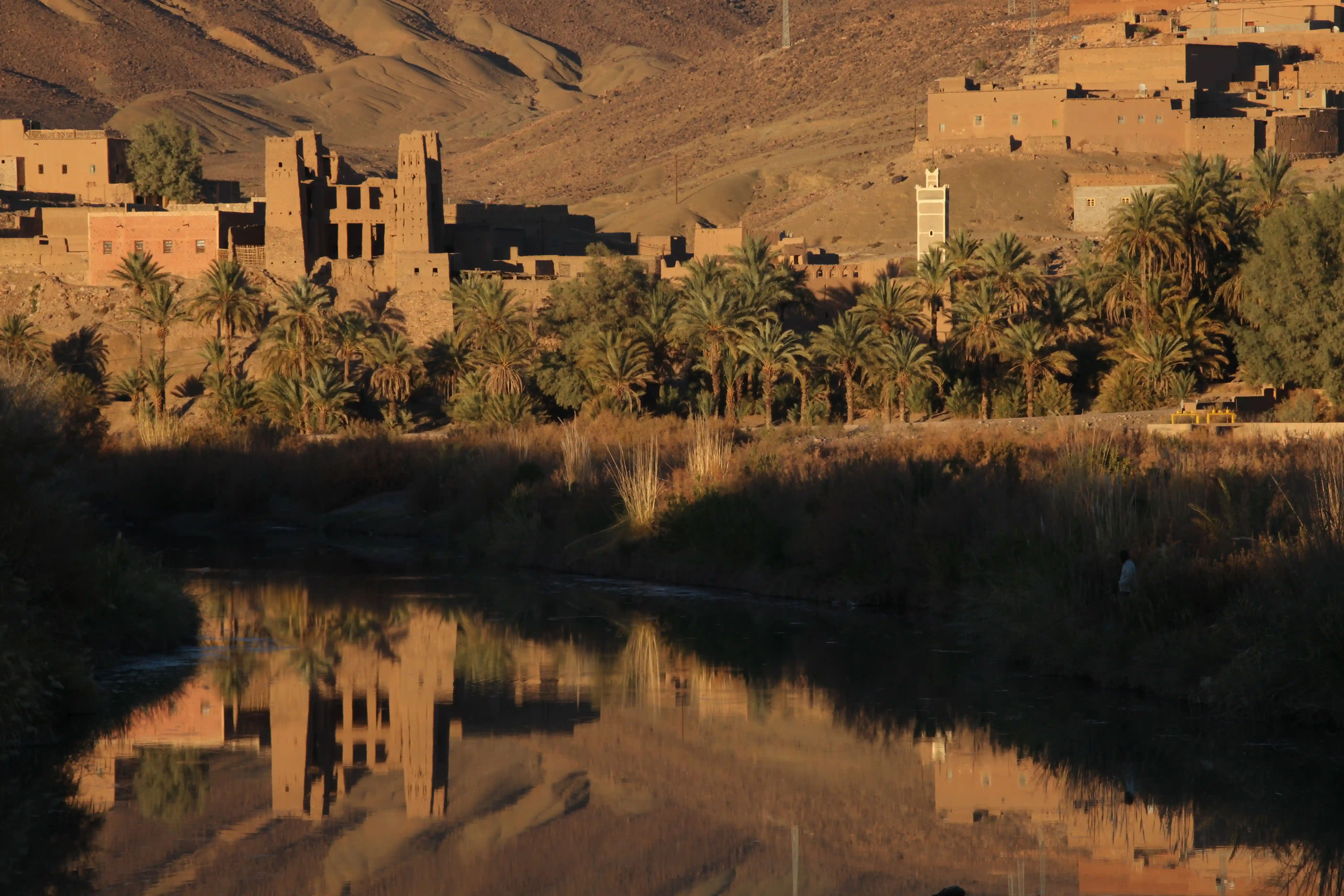 Reflet parfait dans l'eau de kasbahs en pisé, de palmiers et d'un minaret le long de la vallée du Draâ au soleil couchant.