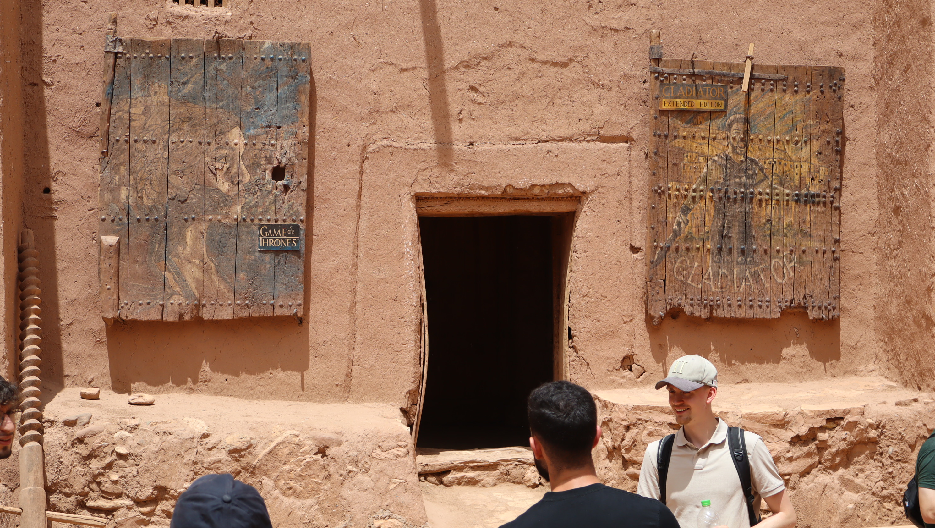 Visiteurs devant un bâtiment en terre à Aït-Ben-Haddou ou Ouarzazate avec des panneaux en bois de Game of Thrones et Gladiator.
