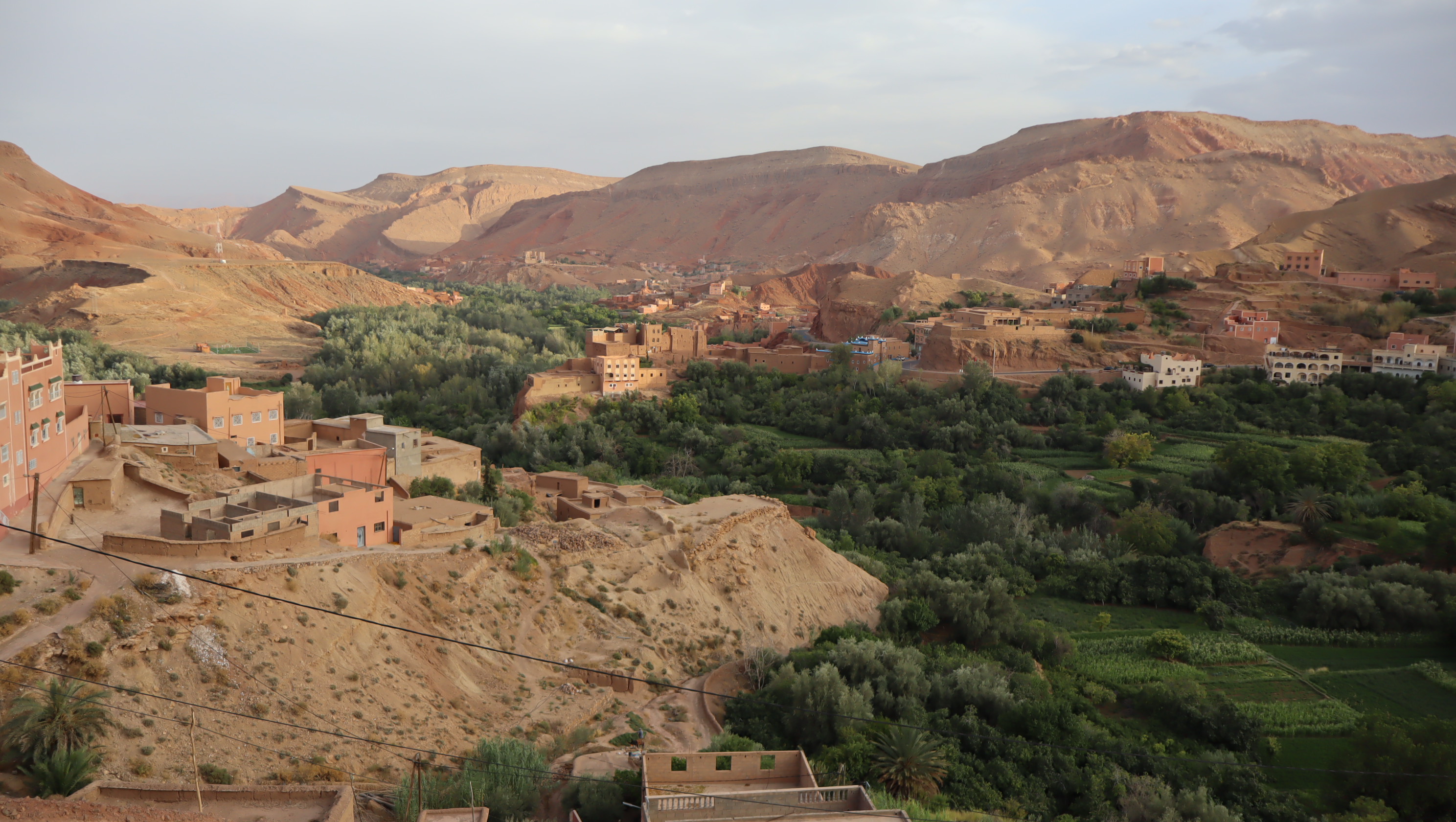 Vue panoramique sur la vallée du Dades ou du Draa au Maroc, montrant un village traditionnel en terre et une palmeraie verdoyante au pied des montagnes.