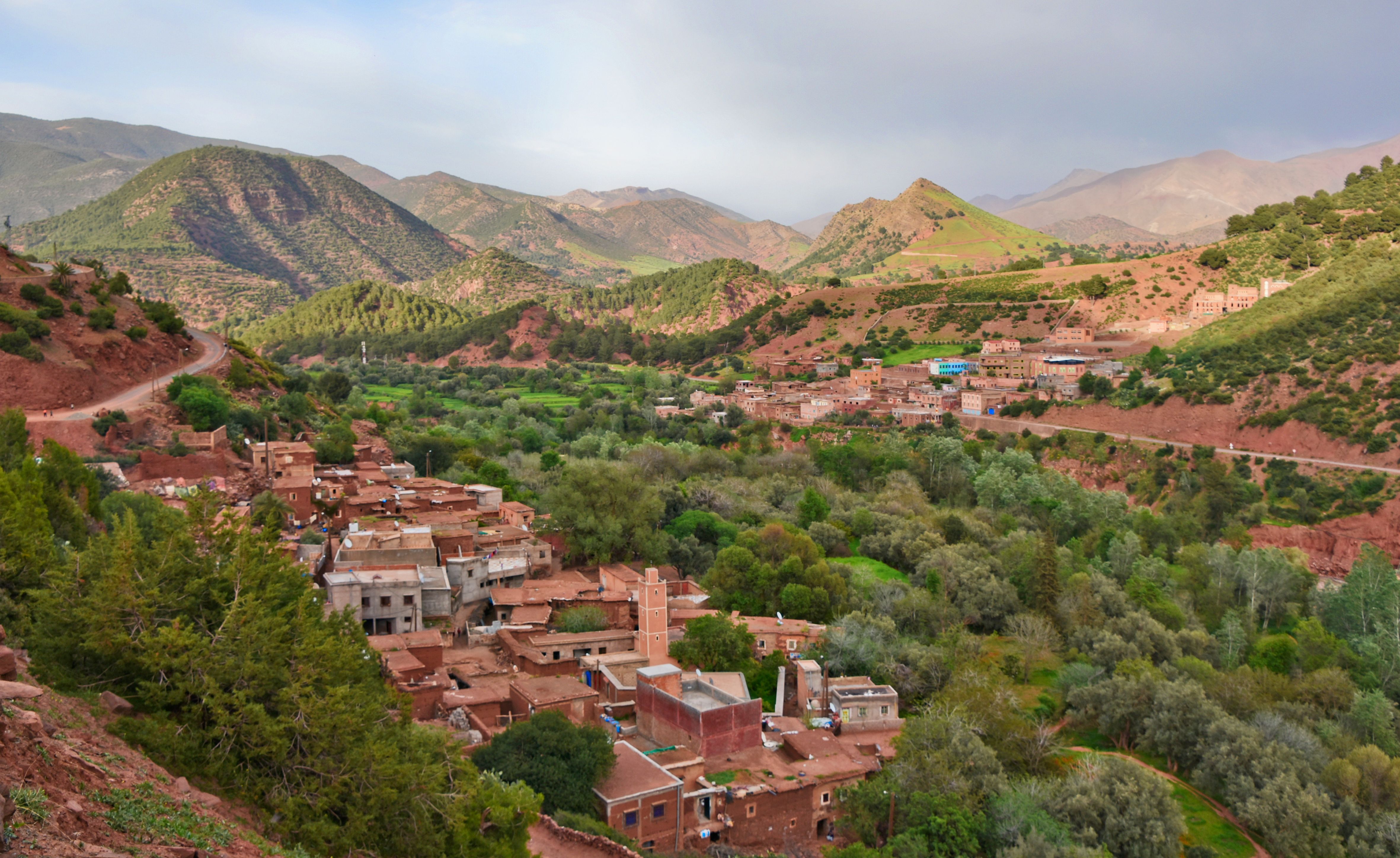 Vue panoramique d'un village berber traditionnel aux maisons en terre rouge, niché dans une vallée verdoyante au pied des montagnes de l'Atlas au Maroc.